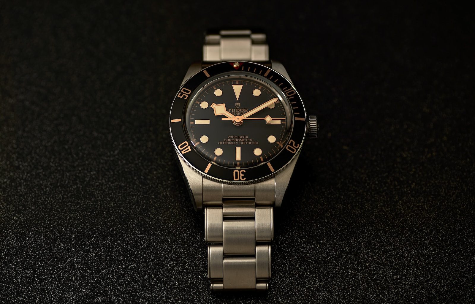 a watch sitting on a black surface with gold numbers