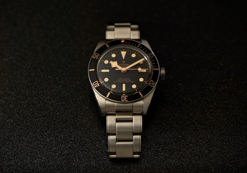 a watch sitting on a black surface with gold numbers