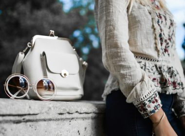 woman wearing beige and red floral top leaning on gray concrete slab with white leather bag ontop