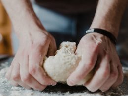 person holding white dough on brown wooden table